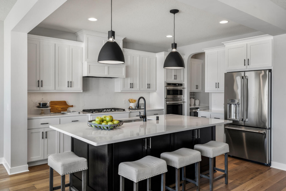 Design ideas for a large transitional l-shaped open plan kitchen in Minneapolis with an undermount sink, shaker cabinets, white cabinets, quartzite benchtops, white splashback, engineered quartz splashback, stainless steel appliances, medium hardwood floors, with island and white benchtop.