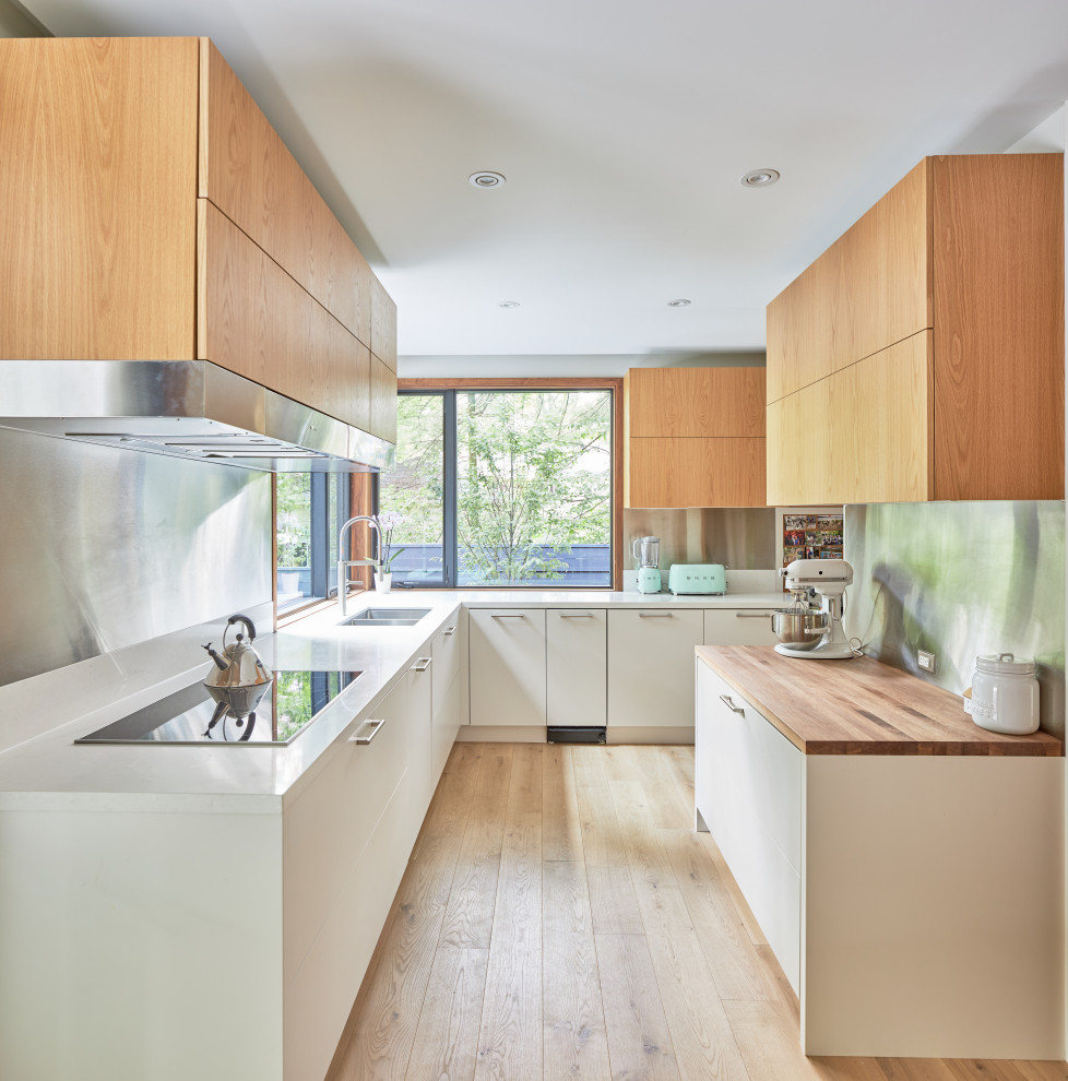 This is an example of a contemporary l-shaped kitchen in Toronto with a double-bowl sink, flat-panel cabinets, white cabinets, metallic splashback, light hardwood floors, beige floor and white benchtop.
