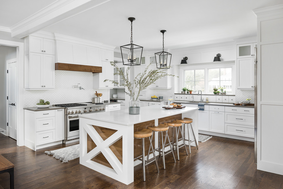 Photo of a country u-shaped eat-in kitchen in Chicago with an undermount sink, shaker cabinets, white cabinets, white splashback, stainless steel appliances, medium hardwood floors, with island, brown floor and white benchtop.