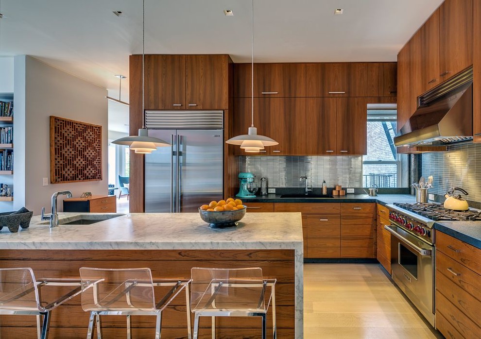 Photo of a midcentury l-shaped kitchen in New York with with island, flat-panel cabinets, medium wood cabinets, matchstick tile splashback, stainless steel appliances, light hardwood floors and metallic splashback.