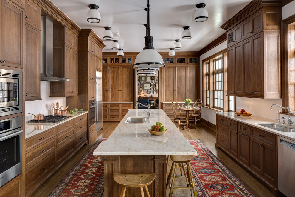 Inspiration for an expansive traditional eat-in kitchen in Columbus with recessed-panel cabinets, ceramic splashback, stainless steel appliances, with island, a double-bowl sink, medium wood cabinets, white splashback, medium hardwood floors and beige benchtop.