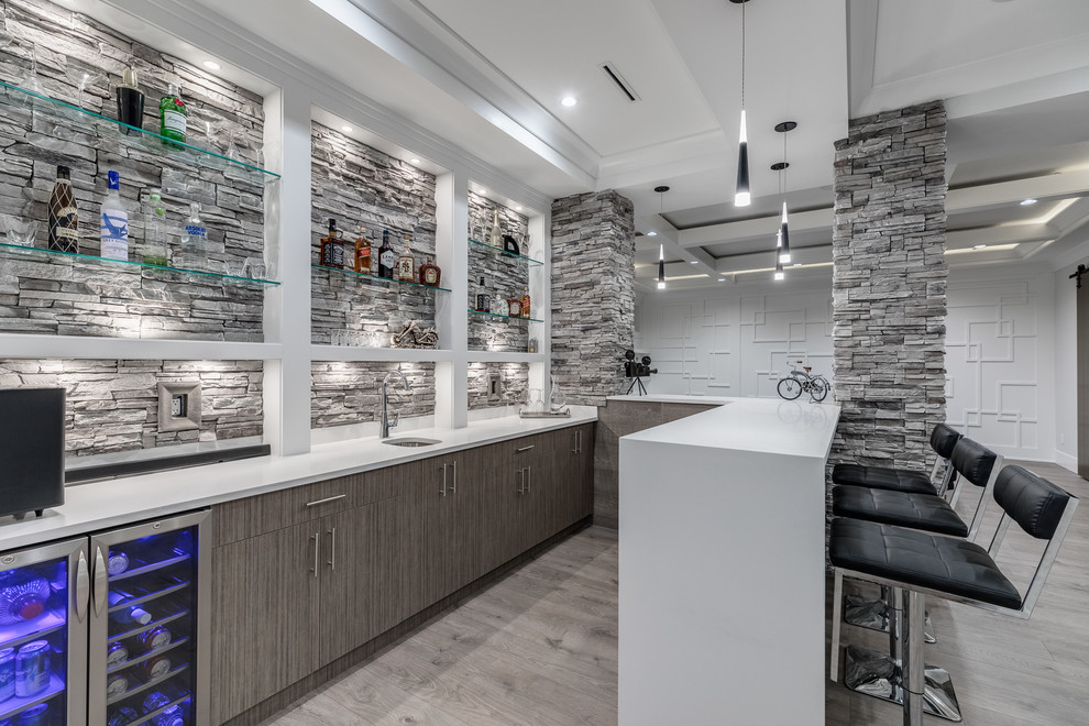 Photo of a mid-sized contemporary u-shaped wet bar in Vancouver with an undermount sink, flat-panel cabinets, grey cabinets, light hardwood floors, grey floor, solid surface benchtops, grey splashback, stone tile splashback and white benchtop.