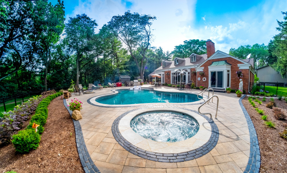 Mid-sized traditional backyard custom-shaped pool in Chicago with a hot tub and natural stone pavers.