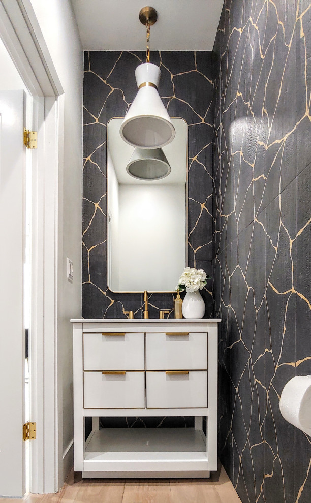 Foto på ett litet funkis vit toalett, med släta luckor, vita skåp, svart kakel, keramikplattor, vita väggar, ljust trägolv, ett undermonterad handfat och bänkskiva i akrylsten