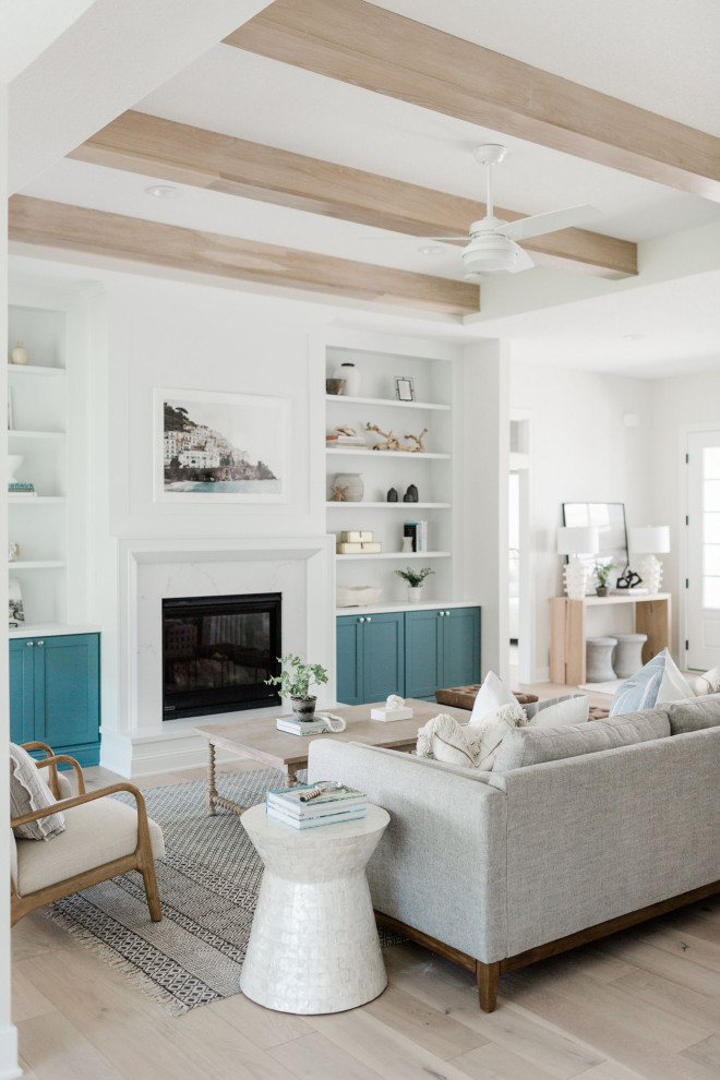 This is an example of a coastal grey and teal living room in Los Angeles with white walls, light hardwood flooring, a standard fireplace, a stone fireplace surround, white floors and exposed beams.