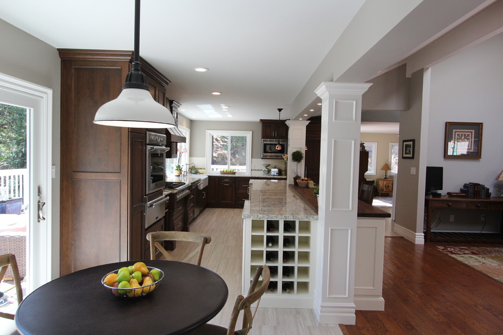 Mid-sized mountain style l-shaped porcelain tile eat-in kitchen photo in San Francisco with a farmhouse sink, recessed-panel cabinets, dark wood cabinets, wood countertops, white backsplash, subway tile backsplash, paneled appliances and an island