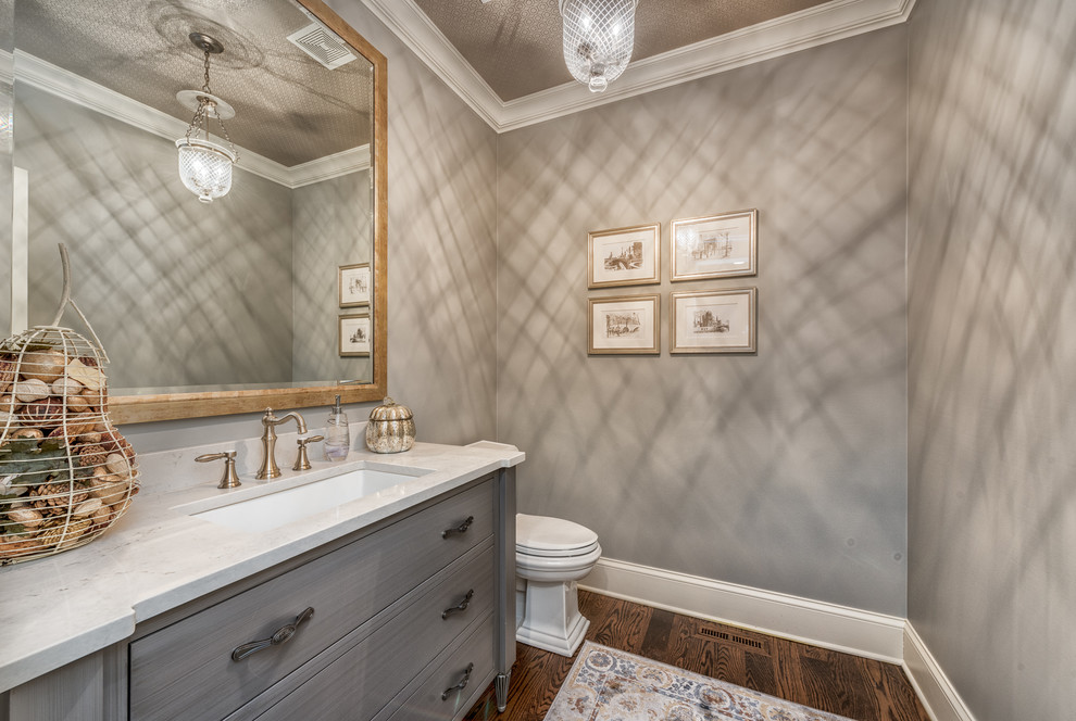 Mid-sized traditional powder room in Chicago with furniture-like cabinets, grey cabinets, a two-piece toilet, grey walls, dark hardwood floors, an undermount sink, engineered quartz benchtops, brown floor and white benchtops.