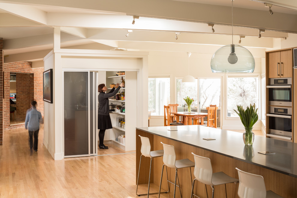 Photo of a midcentury kitchen in Denver with flat-panel cabinets, light wood cabinets, stainless steel appliances, light hardwood floors and with island.