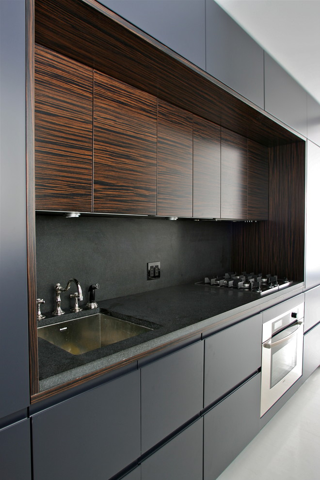 This is an example of a small contemporary single-wall kitchen pantry in New York with an undermount sink, flat-panel cabinets, dark wood cabinets, granite benchtops, black splashback, stone slab splashback and stainless steel appliances.