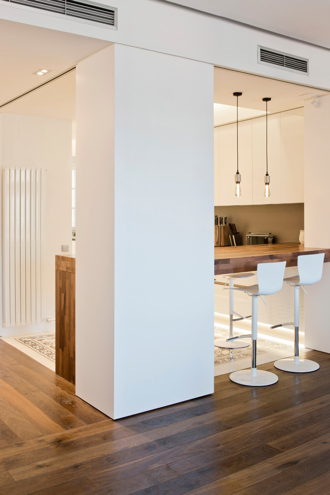 This is an example of a large contemporary u-shaped open plan kitchen in Barcelona with a drop-in sink, flat-panel cabinets, white cabinets, quartz benchtops, brown splashback, panelled appliances, cement tiles, with island, multi-coloured floor and brown benchtop.