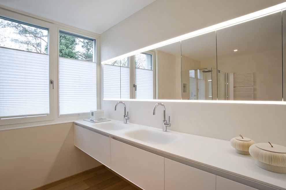 Inspiration for a large contemporary bathroom in Nuremberg with an integrated sink, flat-panel cabinets, white cabinets, a corner shower, beige walls, medium hardwood floors and solid surface benchtops.