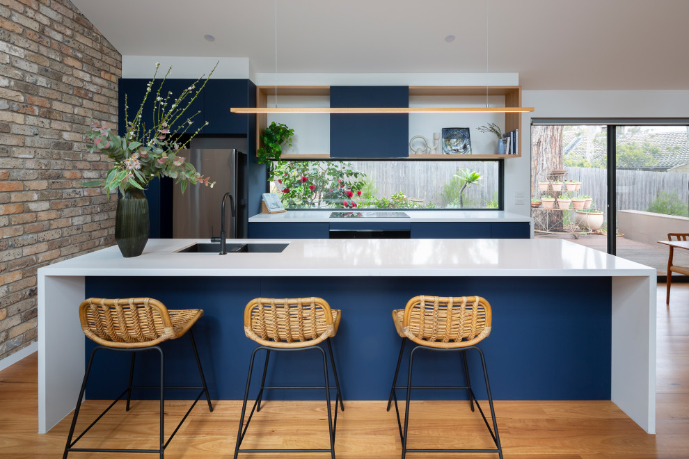 Foto di una cucina minimal di medie dimensioni con lavello sottopiano, ante blu, top in quarzo composito, paraspruzzi a finestra, elettrodomestici neri, pavimento in legno massello medio e top bianco