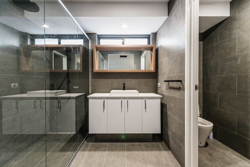 Photo of a mid-sized contemporary master bathroom in Perth with flat-panel cabinets, white cabinets, a curbless shower, a one-piece toilet, gray tile, porcelain tile, grey walls, porcelain floors, a vessel sink and engineered quartz benchtops.