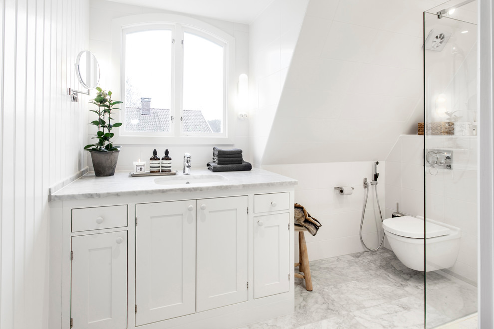 Photo of a mid-sized transitional master bathroom in Gothenburg with shaker cabinets, white cabinets, a wall-mount toilet, white walls, marble floors, marble benchtops, a corner shower, white tile, ceramic tile, a console sink, white floor, a hinged shower door and white benchtops.