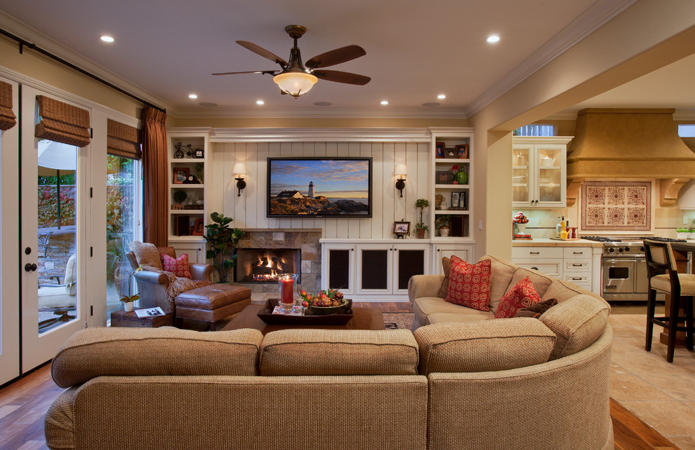Design ideas for a large traditional open concept family room in Orange County with beige walls, medium hardwood floors, a standard fireplace, a stone fireplace surround, a wall-mounted tv and brown floor.
