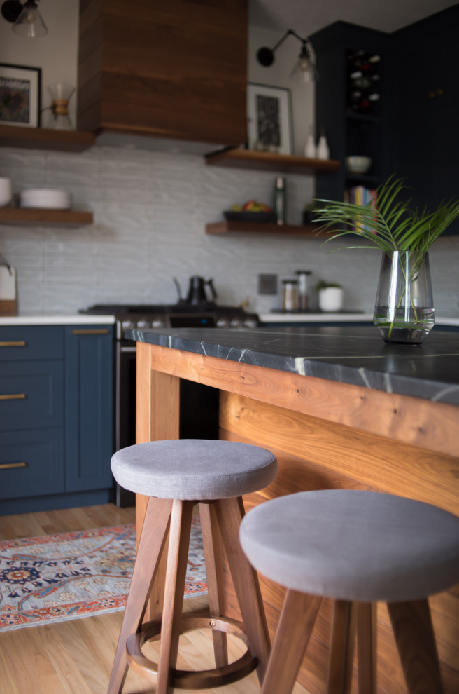 Foto på ett mellanstort vintage svart kök, med skåp i shakerstil, blå skåp, granitbänkskiva, vitt stänkskydd, stänkskydd i keramik, rostfria vitvaror, mellanmörkt trägolv och en köksö