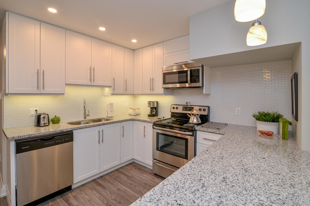 Mid-sized transitional u-shaped medium tone wood floor and gray floor open concept kitchen photo with an undermount sink, shaker cabinets, white cabinets, granite countertops, stainless steel appliances and a peninsula