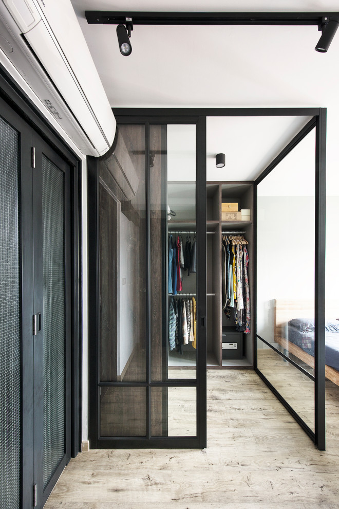 Industrial gender-neutral walk-in wardrobe in Singapore with open cabinets, grey cabinets, light hardwood floors and beige floor.