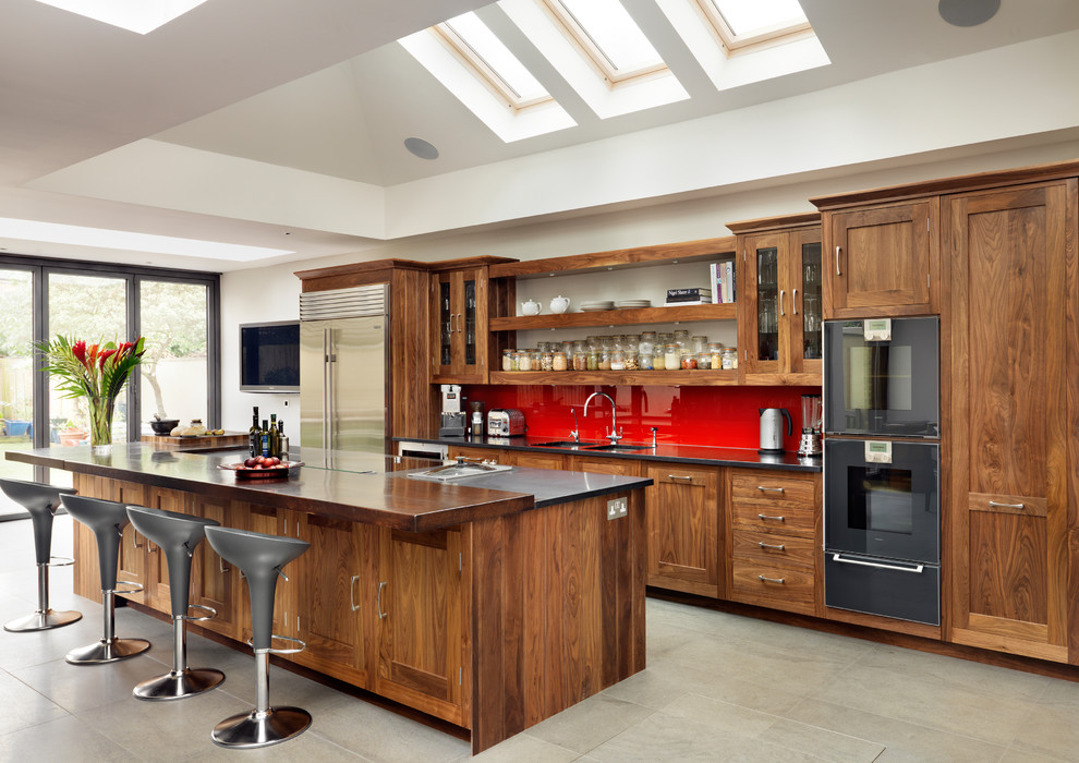 Photo of a traditional kitchen in London with dark wood cabinets, red splashback and black appliances.