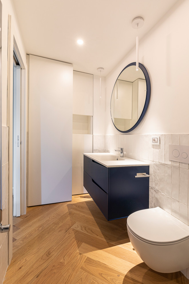Design ideas for a small modern powder room in Milan with flat-panel cabinets, blue cabinets, a two-piece toilet, white tile, ceramic tile, yellow walls, light hardwood floors, an integrated sink, limestone benchtops, beige floor, white benchtops and a freestanding vanity.