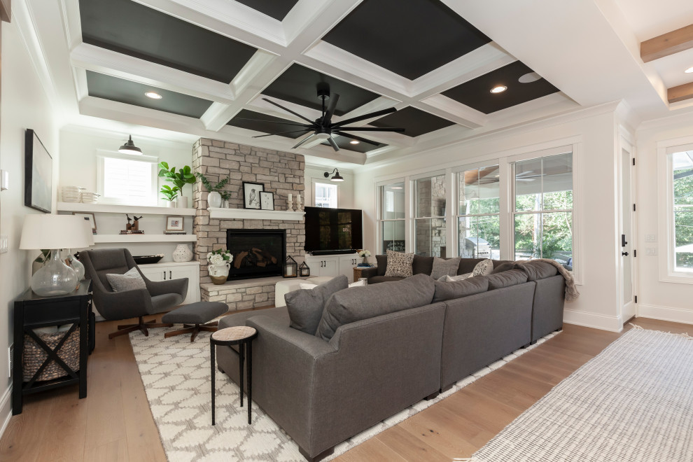 Design ideas for a country open plan games room in Chicago with white walls, medium hardwood flooring, a standard fireplace, a stacked stone fireplace surround, a freestanding tv, brown floors, a coffered ceiling and a chimney breast.