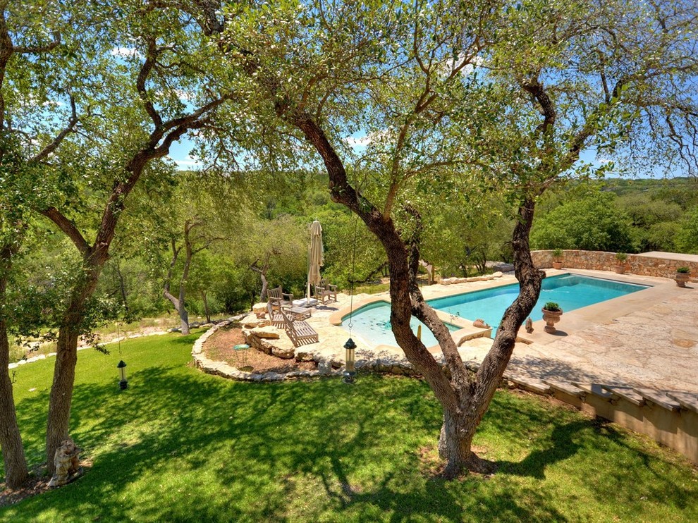 Photo of a large eclectic backyard custom-shaped natural pool in Austin with a water feature and natural stone pavers.