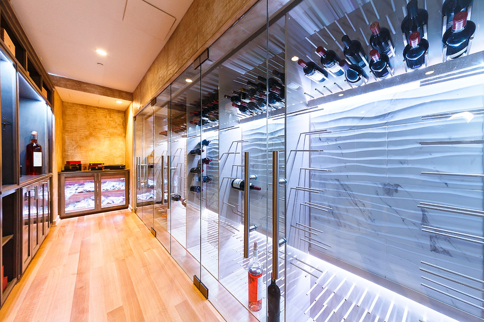 This is an example of a large contemporary wine cellar in New York with light hardwood floors and display racks.