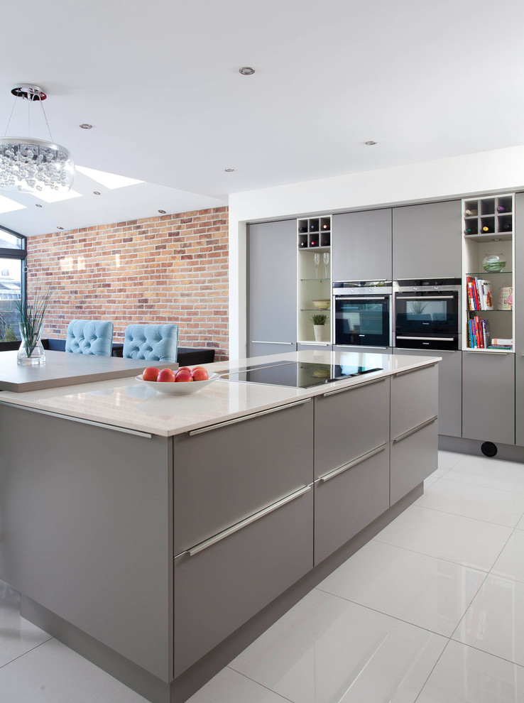 This is an example of a mid-sized contemporary u-shaped open plan kitchen in Dublin with an integrated sink, flat-panel cabinets, grey cabinets, quartzite benchtops, grey splashback, glass sheet splashback, black appliances, cement tiles and with island.