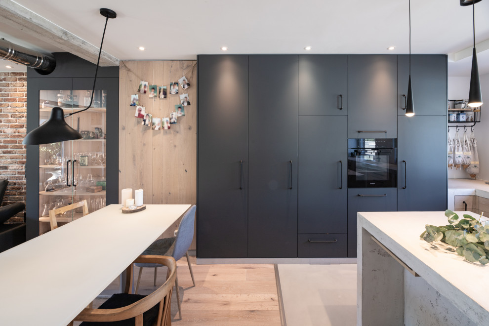 Mid-sized urban galley medium tone wood floor and blue floor eat-in kitchen photo in Other with a double-bowl sink, flat-panel cabinets, black cabinets, concrete countertops, black appliances, an island, gray countertops and black backsplash
