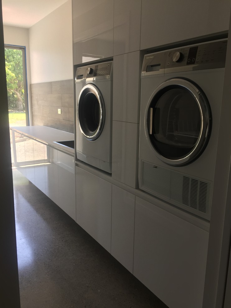 This is an example of a large modern galley separated utility room in Sunshine Coast with a single-bowl sink, white cabinets, engineered stone countertops, grey walls, concrete flooring, a side by side washer and dryer and grey floors.