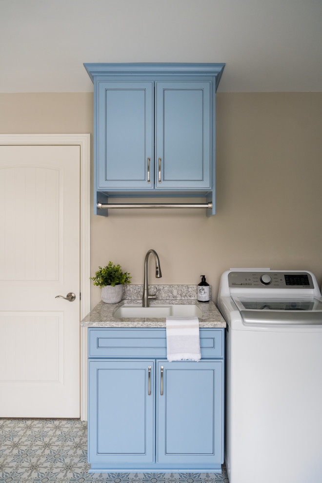 Modern inredning av en mellanstor parallell tvättstuga enbart för tvätt, med en undermonterad diskho, blå skåp, granitbänkskiva, beige väggar, klinkergolv i keramik och en tvättmaskin och torktumlare bredvid varandra