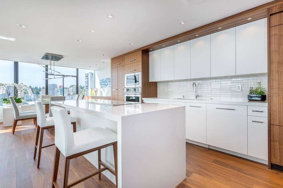 Inspiration for a mid-sized transitional galley medium tone wood floor open concept kitchen remodel in Vancouver with an undermount sink, flat-panel cabinets, medium tone wood cabinets, quartz countertops, white backsplash, ceramic backsplash, stainless steel appliances and an island
