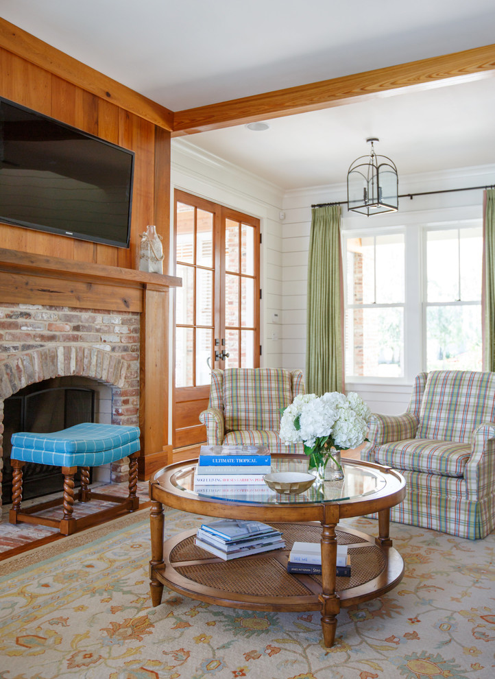 Example of a beach style medium tone wood floor and brown floor living room design in Jacksonville with white walls, a standard fireplace, a brick fireplace and a wall-mounted tv