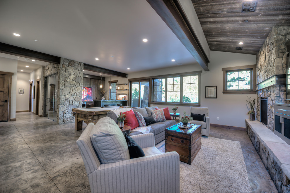 Large transitional open concept family room with a game room, concrete floors, a hanging fireplace, a stone fireplace surround and a freestanding tv.