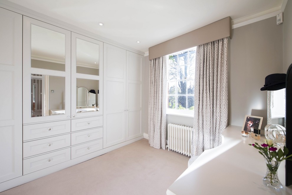 Mid-sized traditional women's dressing room in London with shaker cabinets, white cabinets, carpet and beige floor.