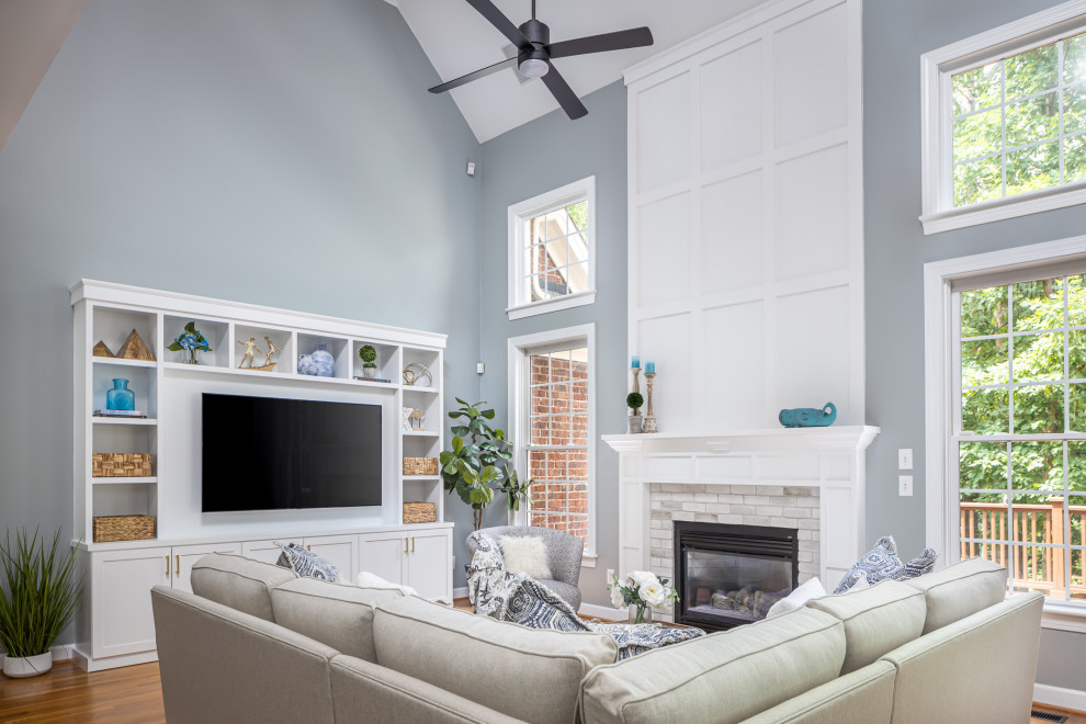 ローリーにある高級な中くらいなトラディショナルスタイルのおしゃれなLDK (青い壁、無垢フローリング、吊り下げ式暖炉、木材の暖炉まわり、埋込式メディアウォール、茶色い床、三角天井) の写真