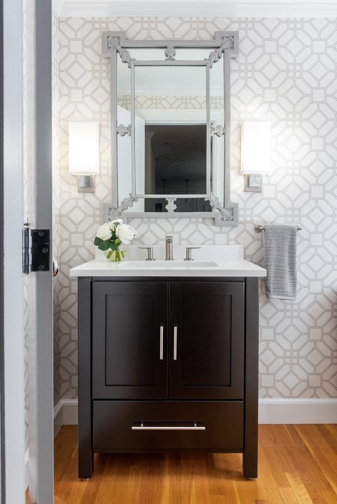 Photo of a mid-sized transitional powder room in Boston with black cabinets, grey walls, medium hardwood floors, an undermount sink, brown floor, white benchtops, furniture-like cabinets and engineered quartz benchtops.