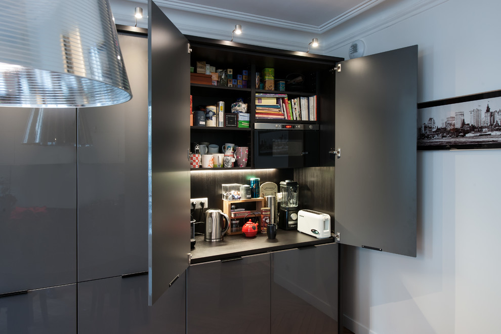 Photo of a mid-sized contemporary galley separate kitchen in Other with a single-bowl sink, beaded inset cabinets, grey cabinets, laminate benchtops, white splashback, porcelain splashback, black appliances, medium hardwood floors and no island.