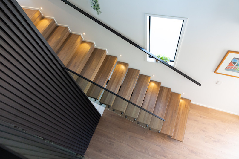 Medium sized modern wood floating metal railing staircase in Auckland with open risers.
