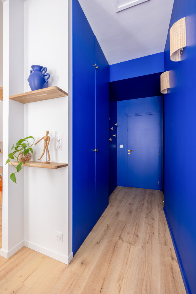 Aménagement d'une petite entrée bord de mer avec un couloir, un mur bleu, parquet clair, une porte simple et une porte bleue.