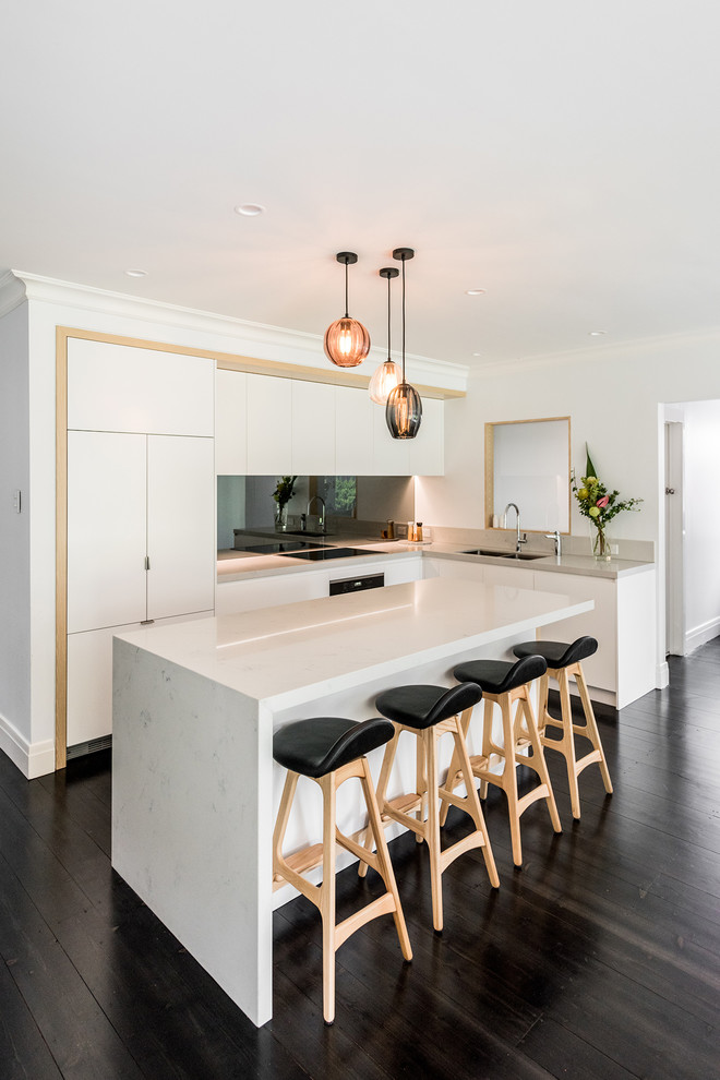 This is an example of a large contemporary l-shaped open plan kitchen in Melbourne with an undermount sink, flat-panel cabinets, white cabinets, quartz benchtops, metallic splashback, mirror splashback, black appliances, dark hardwood floors, with island and brown floor.
