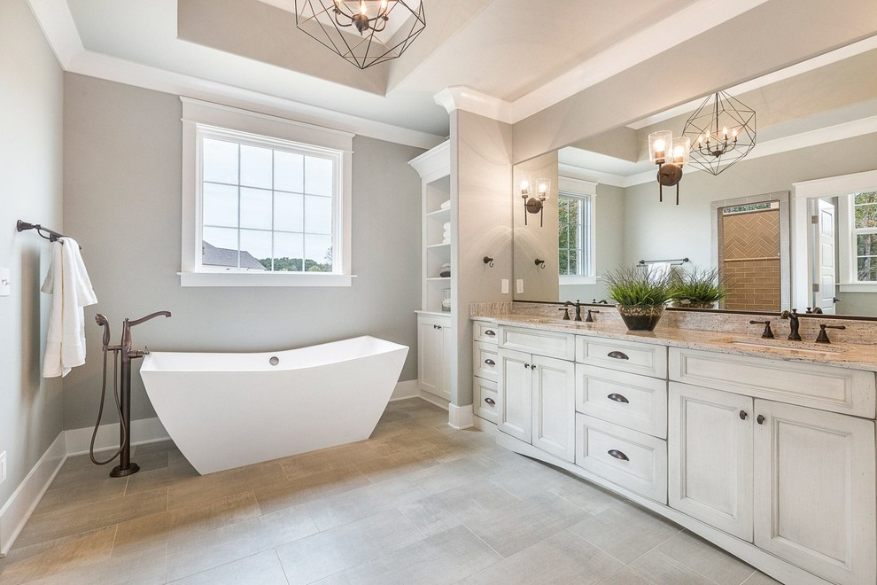 This is an example of a mid-sized country master bathroom in Raleigh with flat-panel cabinets, white cabinets, a freestanding tub, grey walls, porcelain floors, granite benchtops, grey floor and white benchtops.