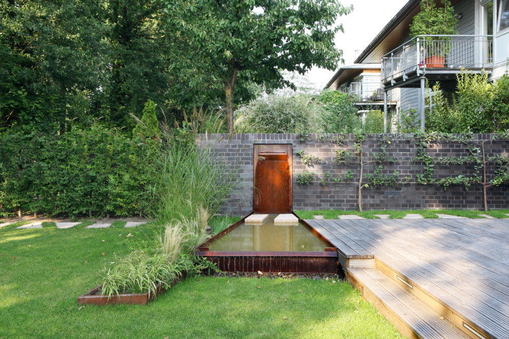Cette image montre un petit jardin à la française latéral minimaliste avec une cascade et une terrasse en bois.