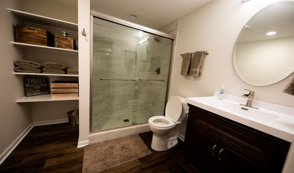 Alcove shower - mid-sized transitional 3/4 gray tile and porcelain tile dark wood floor and brown floor alcove shower idea in Chicago with raised-panel cabinets, dark wood cabinets, a two-piece toilet, beige walls, an integrated sink, solid surface countertops and white countertops
