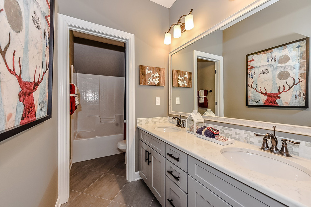 Inspiration for a mid-sized transitional bathroom in Charlotte with recessed-panel cabinets, grey cabinets, a freestanding tub, a shower/bathtub combo, gray tile, porcelain tile, grey walls, porcelain floors, quartzite benchtops, a shower curtain, a two-piece toilet, an undermount sink and brown floor.