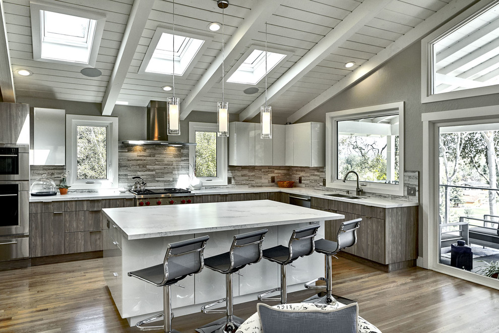 Inspiration for a large contemporary l-shaped open plan kitchen in San Francisco with an undermount sink, flat-panel cabinets, grey cabinets, quartz benchtops, grey splashback, travertine splashback, stainless steel appliances, light hardwood floors, with island, brown floor and grey benchtop.