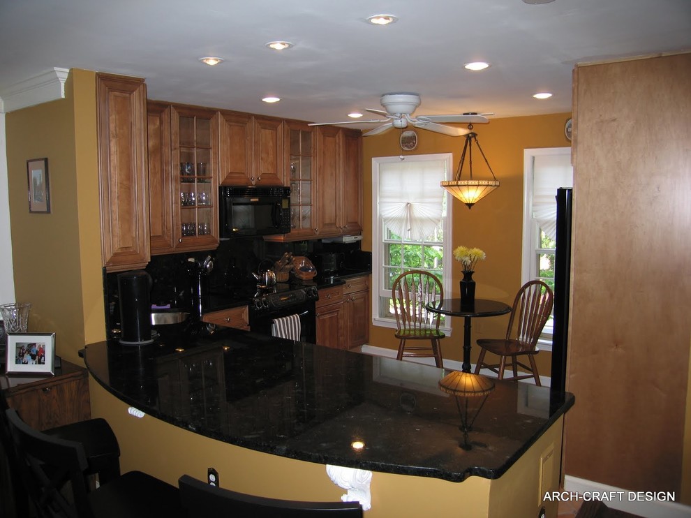 Photo of a small traditional single-wall eat-in kitchen in DC Metro with raised-panel cabinets, medium wood cabinets, granite benchtops, black splashback, stone slab splashback, black appliances, porcelain floors, an undermount sink and a peninsula.