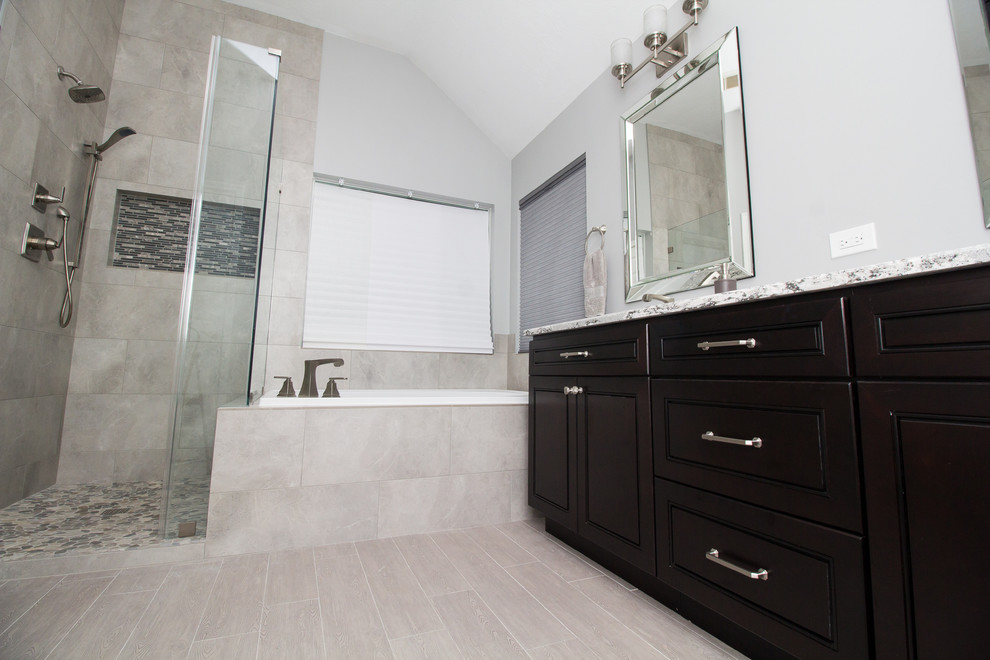 This is an example of a mid-sized transitional master bathroom in Houston with dark wood cabinets, a drop-in tub, a corner shower, gray tile, porcelain tile, grey walls, porcelain floors, an undermount sink, engineered quartz benchtops, grey floor, a hinged shower door and beaded inset cabinets.