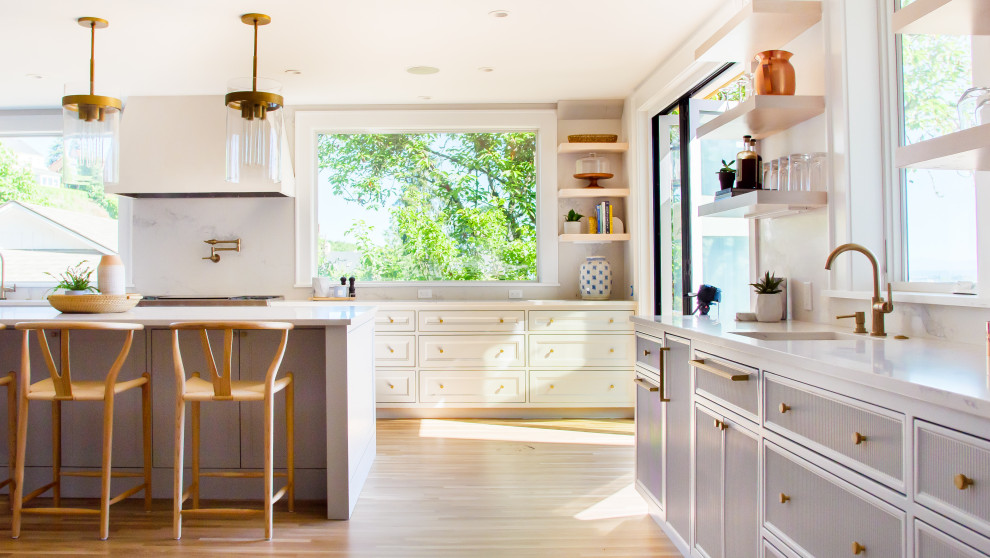 Diseño de cocina clásica renovada grande con puertas de armario blancas, electrodomésticos de acero inoxidable, suelo de madera clara y encimeras blancas