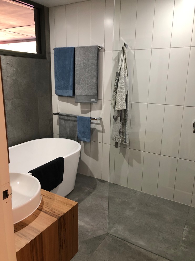 Inspiration for a small modern master bathroom with furniture-like cabinets, brown cabinets, a freestanding tub, an open shower, gray tile, ceramic tile, white walls, ceramic floors, a vessel sink, wood benchtops, grey floor and brown benchtops.